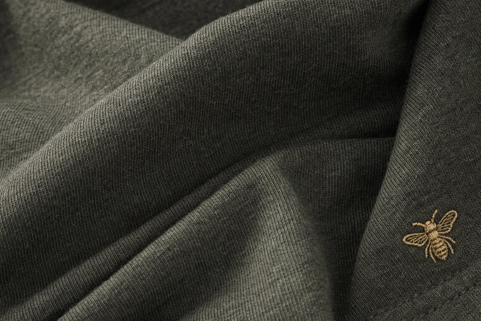 Macro detail of Field Olive fabric with honey-gold bee embroidery.